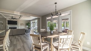 A spacious dining area with a large wooden table and chairs, a chandelier, and a view of the outdoors through large windows. - Private Paradise 2 Story Dock, Beach, Hot Tub (Mineral)