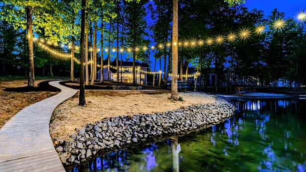 A pathway leading to a lakeside area with string lights and a wooden dock. - Private Paradise 2 Story Dock, Beach, Hot Tub (Mineral)