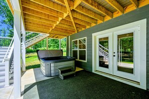 A covered outdoor area with a hot tub, a staircase, and a door leading to a covered porch.