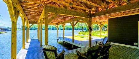 Terraza cubierta al aire libre con vigas de madera, asientos y vista a un cuerpo de agua.