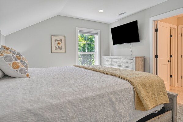 A bedroom with a bed, a television mounted on the wall, a window, and a door.
