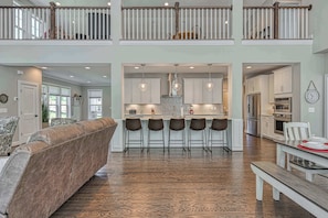 A spacious living area with a high ceiling, a kitchen with modern appliances, and a dining area with a bench.