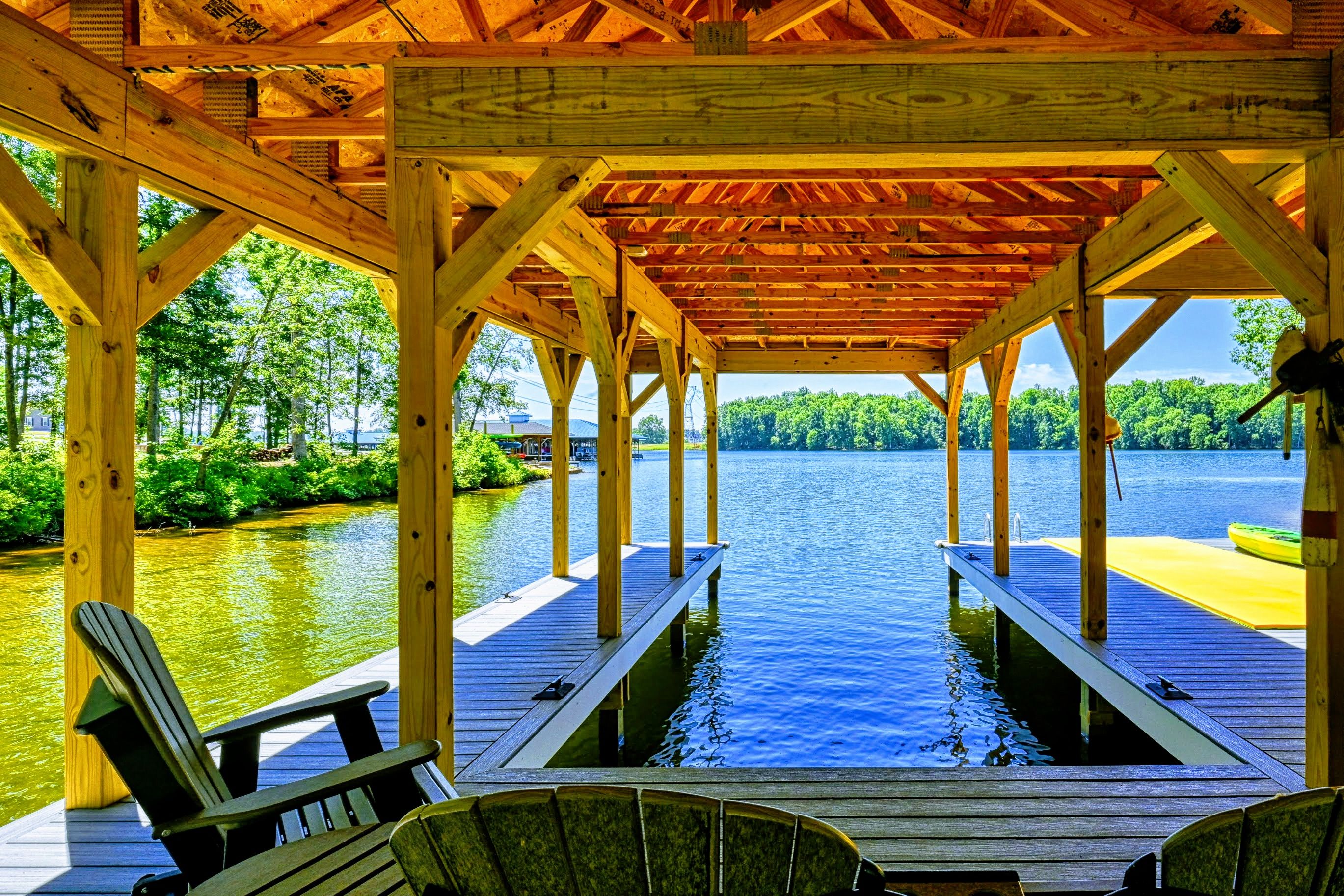 A wooden deck with chairs overlooking a calm lake, surrounded by lush greenery.