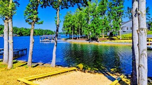 A lakeside area with a wooden deck, a sandy area, and trees. - Private Cove Lakefront Lake Anna Beach & Dock (Mineral)