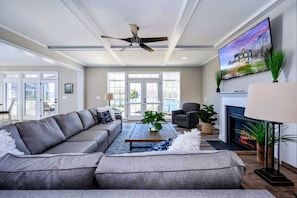 A modern living room with a sectional sofa, a fireplace, a television, and a ceiling fan.