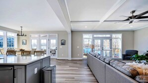 A spacious kitchen with a central island, a dining area with chairs, a large grey sofa, and a ceiling fan. - Private Cove Lakefront Lake Anna Beach & Dock (Mineral)