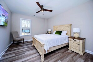 A bedroom with a bed, a chair, a nightstand, a lamp, a ceiling fan, and a window.