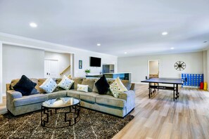 Una sala moderna con un sofá modular, una mesa de centro, una mesa de ping pong y una cocina al fondo.