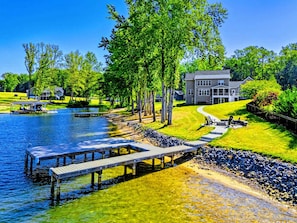 A lakeside property with a dock, a walking path, and a large house with a lawn.