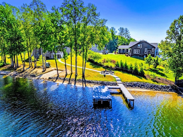 A lakeside property with a dock, a grassy area, and a house in the background.