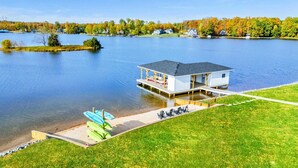 Eine Holzhütte am Seeufer mit Anlegesteg, Rasenfläche und Boot.