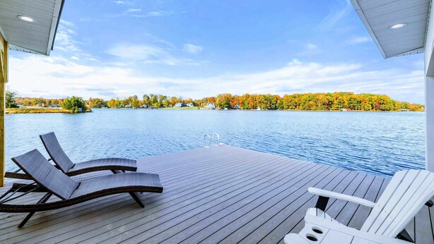 Eine Holzterrasse mit Liegestühlen mit Blick auf einen See, umgeben von Herbstlaub.