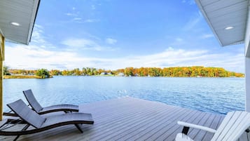Une terrasse en bois avec des chaises longues donnant sur un lac, entourée d’un paysage automnal.