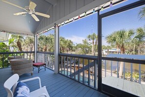 A covered outdoor area with a ceiling fan, a table with chairs, and a view of palm trees and water. - Gorgeous Near Beach Pool Home in West Rocks (Sanibel)