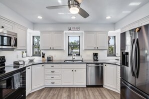 Une cuisine moderne avec des meubles blancs, des appareils en acier inoxydable, un lave-vaisselle et un ventilateur de plafond.