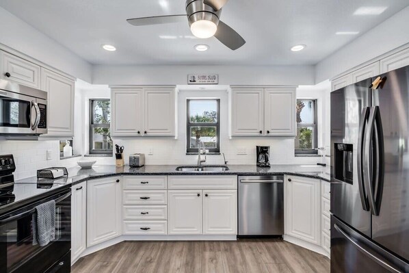 A modern kitchen with white cabinetry, stainless steel appliances, a dishwasher, and a ceiling fan. - Gorgeous Near Beach Pool Home in West Rocks (Sanibel)