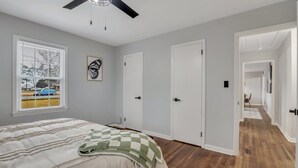 Een slaapkamer met een bed, een plafondventilator, een raam met zonwering, en een deur naar een andere kamer.