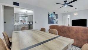 Een moderne woonkamer met een grote houten eettafel, een leren bank en een flatscreen televisie.