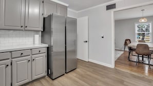 Een moderne keuken met grijze kastjes, een roestvrijstalen koelkast en een eethoek met tafel en stoelen.