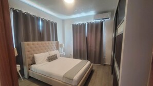A modern bedroom with a large bed, a bedside table with a lamp, and curtains. - Spacious 3BD Beach House 2 Blocks from Ocean Park (San Juan)