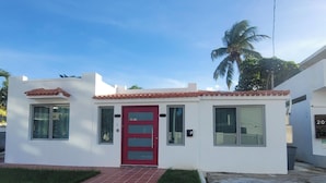 A small, single-story building with a red door, numbered 2058, and a tiled entrance.