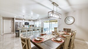 Un comedor con una mesa de madera dispuesta para cuatro personas, rodeada de sillas, y una cocina al fondo.