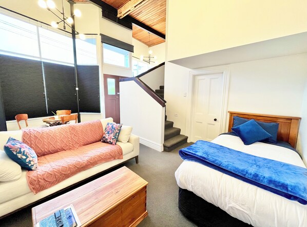 Ein modernes Zimmer mit einer Couch, einem Bett, einer Holzbank und einer Treppe.