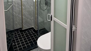 Un baño moderno con ducha acristalada, inodoro y una pequeña ventana.