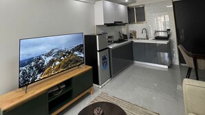 Una sala de estar moderna con un televisor de pantalla plana, una mesa de centro oscura y una zona de cocina con armarios y estufa.