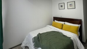 Un dormitorio con una cama, una manta verde y dos cuadros en la pared.