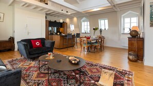 Un vaste espace de vie doté d’un haut plafond, une cuisine à l’arrière-plan et un coin repas avec une table et des chaises.