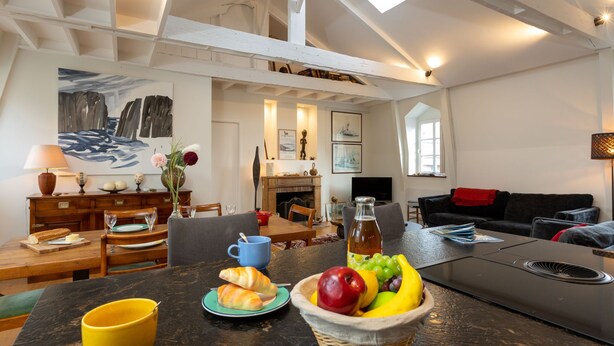Un vaste espace de vie comprenant un coin repas avec une table préparée pour le petit-déjeuner, un canapé confortable et une cheminée.