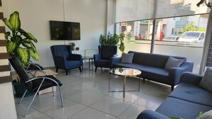 Un vestíbul d'hotel modern amb un sofà, cadires, una taula de cafè i grans finestres que donen vista al carrer.