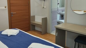 Habitació d'hotel amb un llit, escriptori, televisió penjada a la paret i un bany visible a través d'una porta oberta.