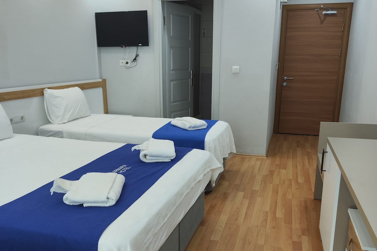 A hotel room with three beds, wooden flooring, a TV mounted on the wall, and a door leading to a bathroom.