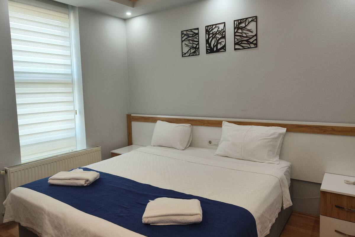 A bedroom with a bed, bedside tables, and a window with blinds.