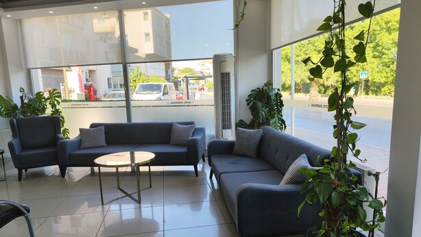 Un vestíbul d'hotel modern amb un sofà gris, una taula rodona petita i plantes en testos.
