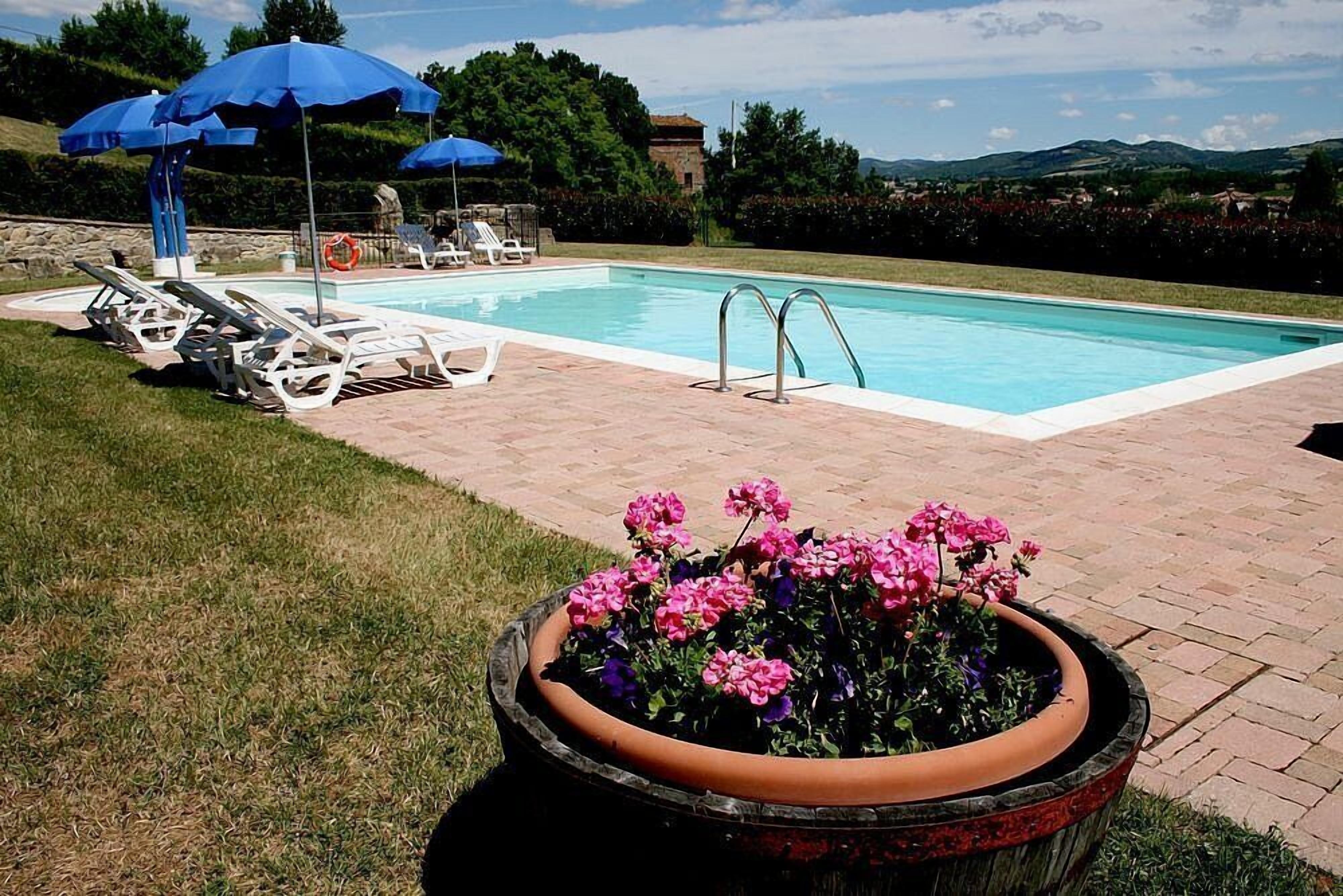 Une piscine entourée d’un patio en briques et d’un parterre de fleurs, avec des chaises longues et des parasols.