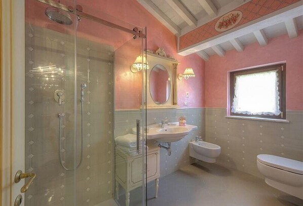 Un baño con ducha envuelta en vidrio, un lavabo, un inodoro y un ventanal con marco decorativo.