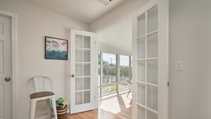 Ein helles Zimmer mit Holzboden, einem weißen Stuhl, einem Korb mit Spielzeug und einem großen Fenster mit Blick auf Grünflächen.