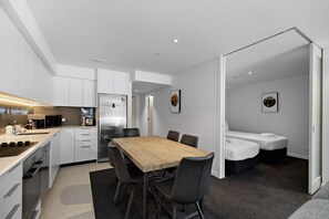 Kompakti hotellihuone, jossa on pieni keittiö, ruokailutila ja kaksi erillistä sänkyä.