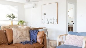 A modern living room with a brown leather sofa, a blue armchair, and a dining area with a wooden table. - Modern coastal charm in Kingscliff! (Tweed)