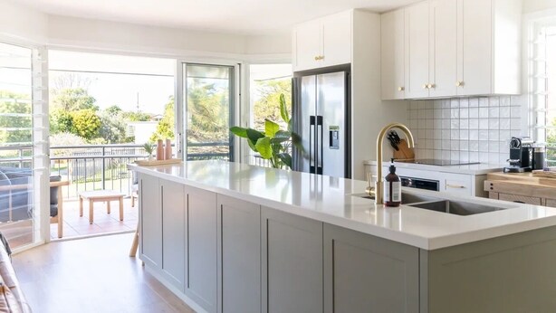 A modern kitchen with a large island, white cabinetry, and a view to the outside. - Modern coastal charm in Kingscliff! (Tweed)