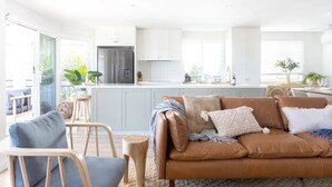 A modern kitchen with white cabinets, a stainless steel refrigerator, and a dining area with a table and chairs. - Modern coastal charm in Kingscliff! (Tweed)