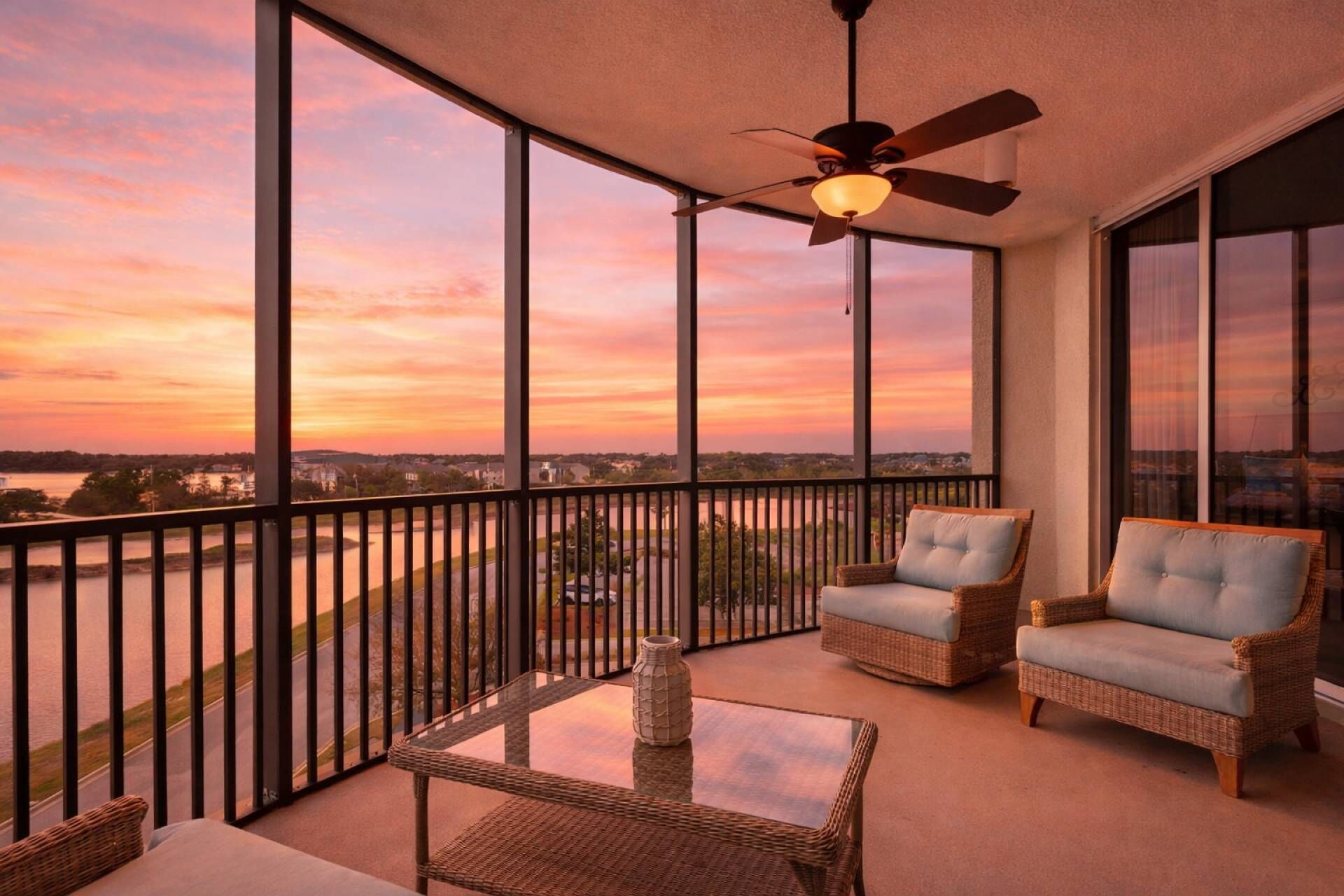 A balcony with wicker furniture, a ceiling fan, and a view of a sunset over a body of water.