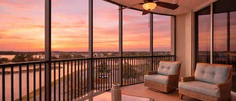 Ein Balkon mit Korbmöbeln, einem Deckenventilator und Blick auf einen Sonnenuntergang über dem Wasser.