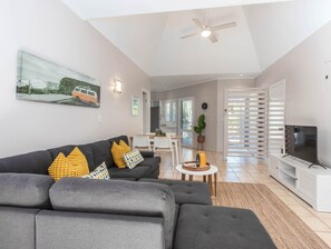 A modern living room with a sectional sofa, a flat-screen TV, and a ceiling fan. - 3 Bedroom Hastings Cove Villa! (Tweed)
