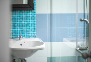 Ein Badezimmer mit einem weißen Waschbecken, blau-weißen Fliesen und einer Duschkabine aus Glas.