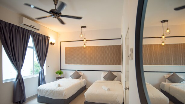 Een hotelkamer met twee bedden, een plafondventilator, een grote spiegel en een raam met gordijnen.