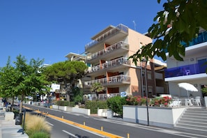 Un immeuble à plusieurs étages doté de balcons, une rue avec une ligne médiane jaune et quelques espaces verts.
